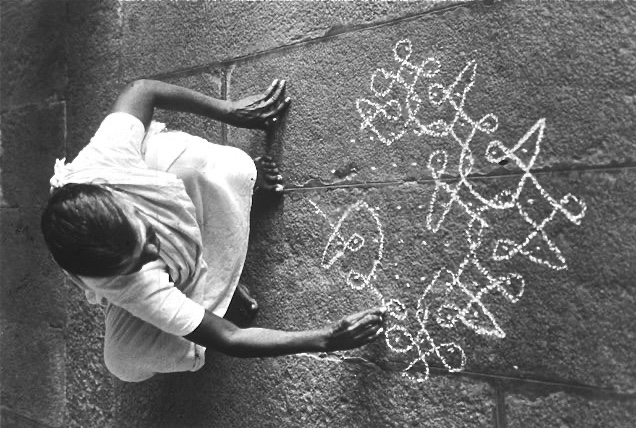 woman drawing kolam on ground